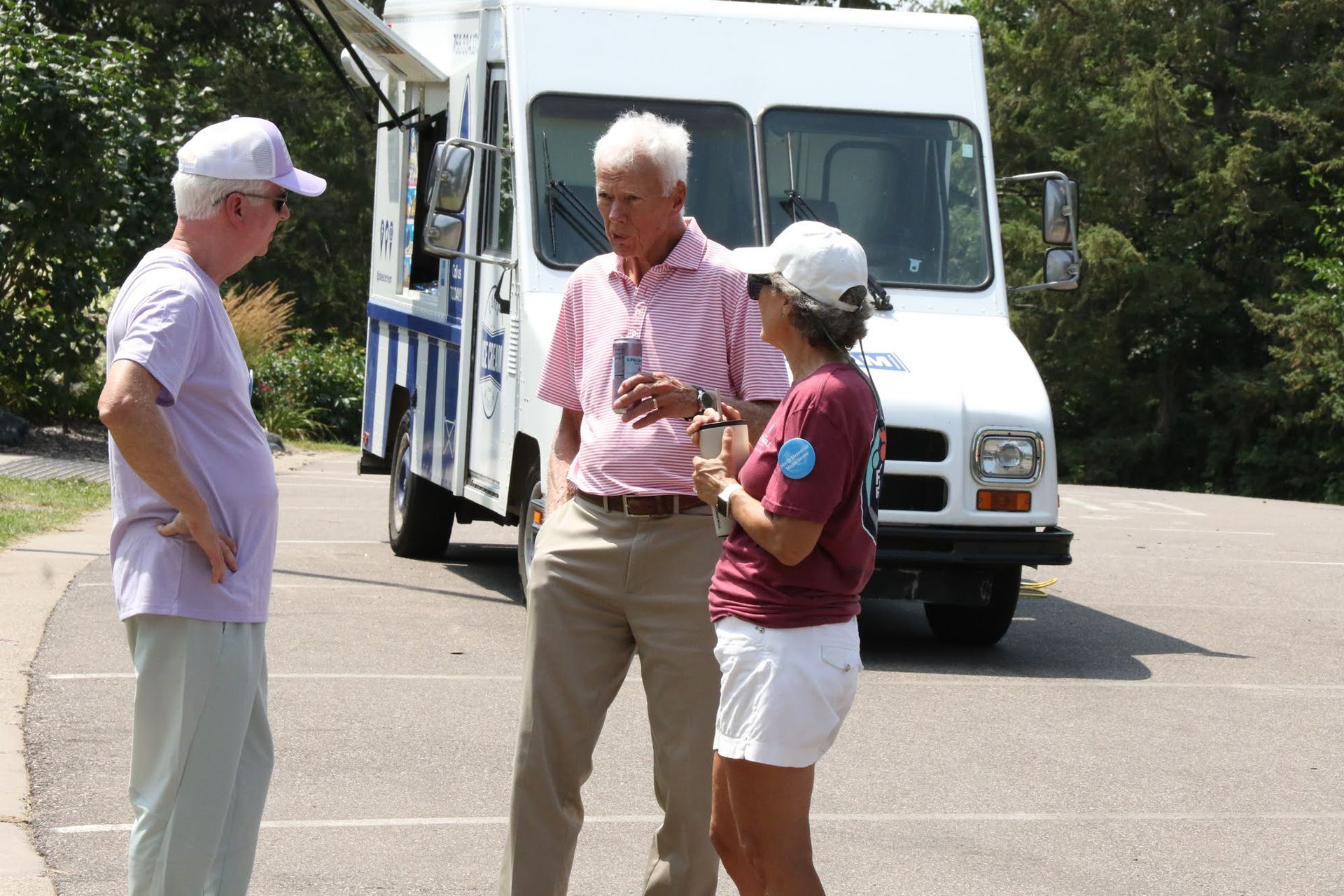 Three people talking near a white food truck in a parking lot on a sunny day.