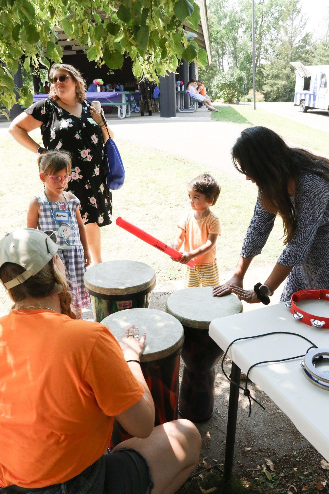 People playing drums at an outdoor event, with children and adults.