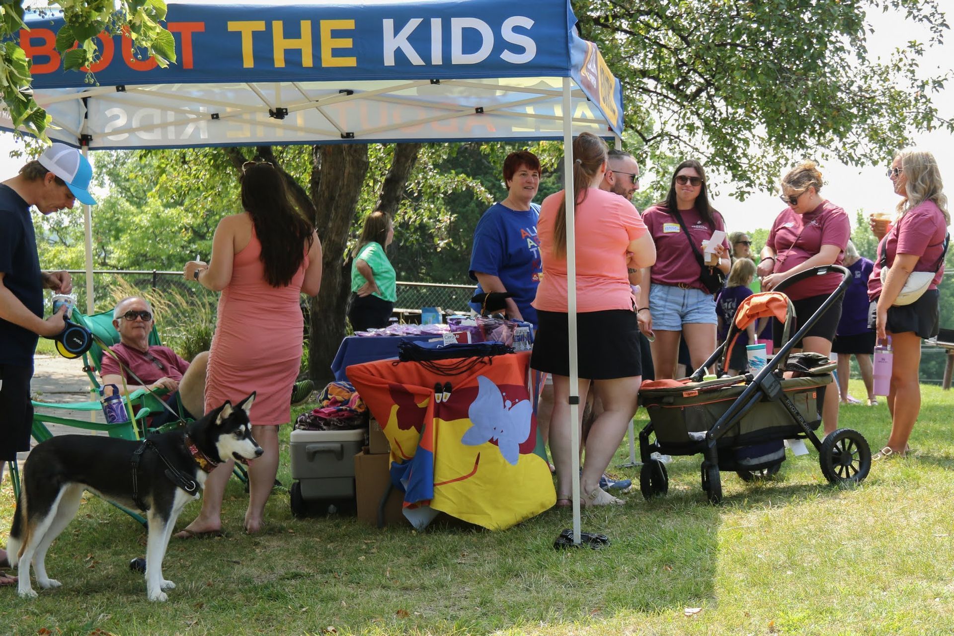 People at an outdoor event with a booth under a tent labeled 