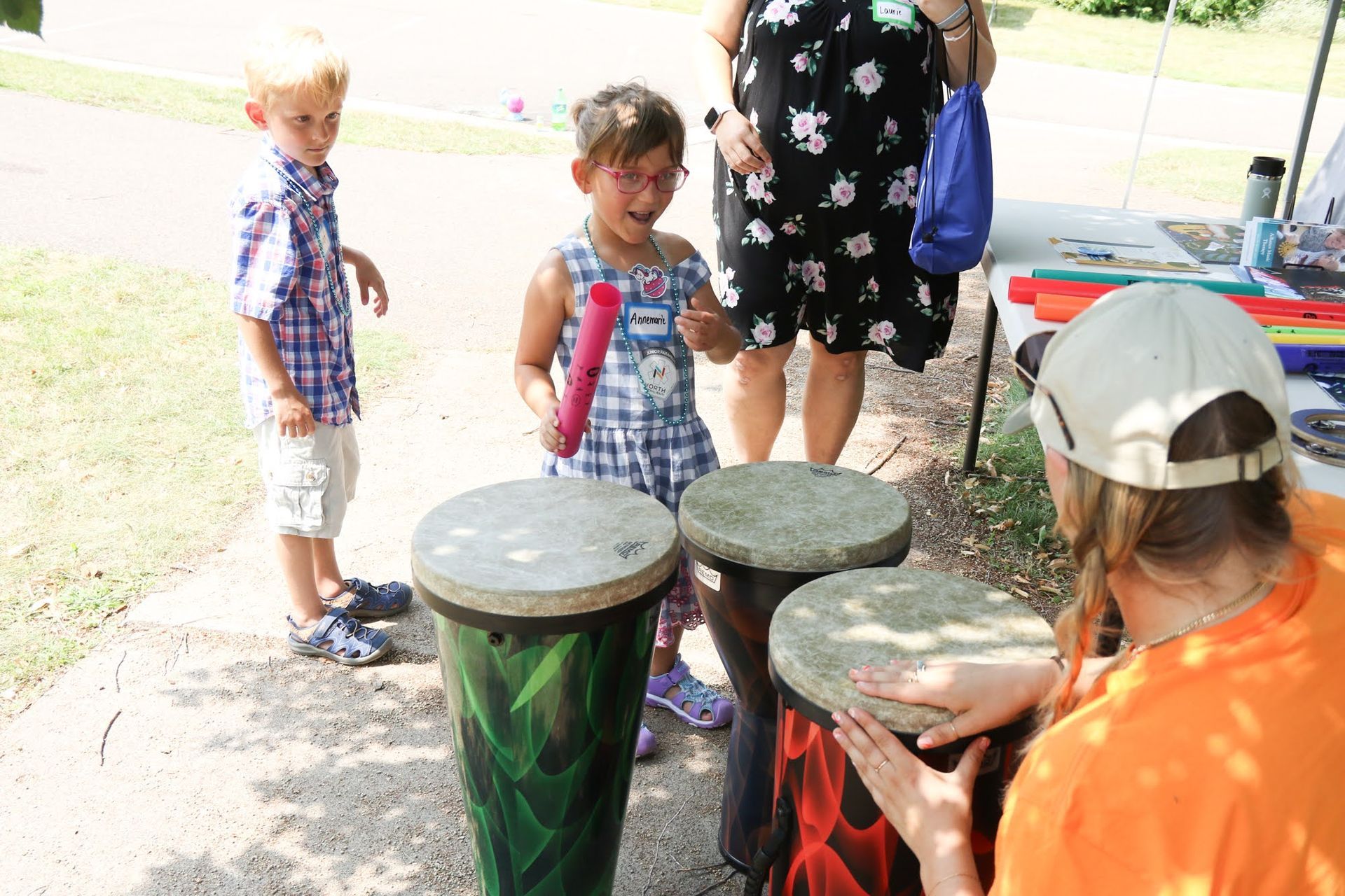 Children playing drums at an outdoor event, attended by an adult.