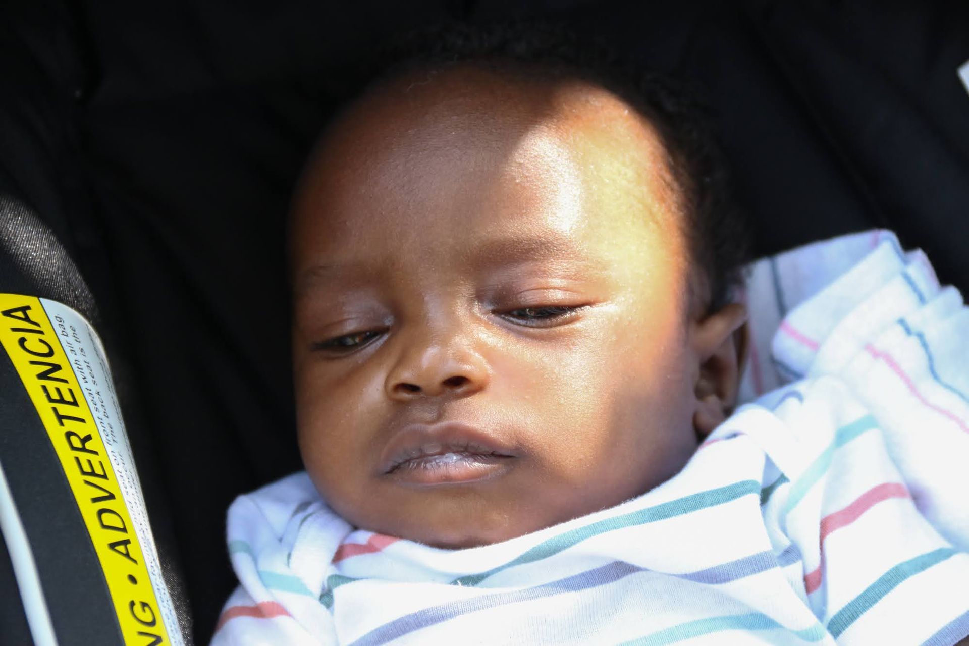 Baby in a striped onesie, resting in a black stroller.