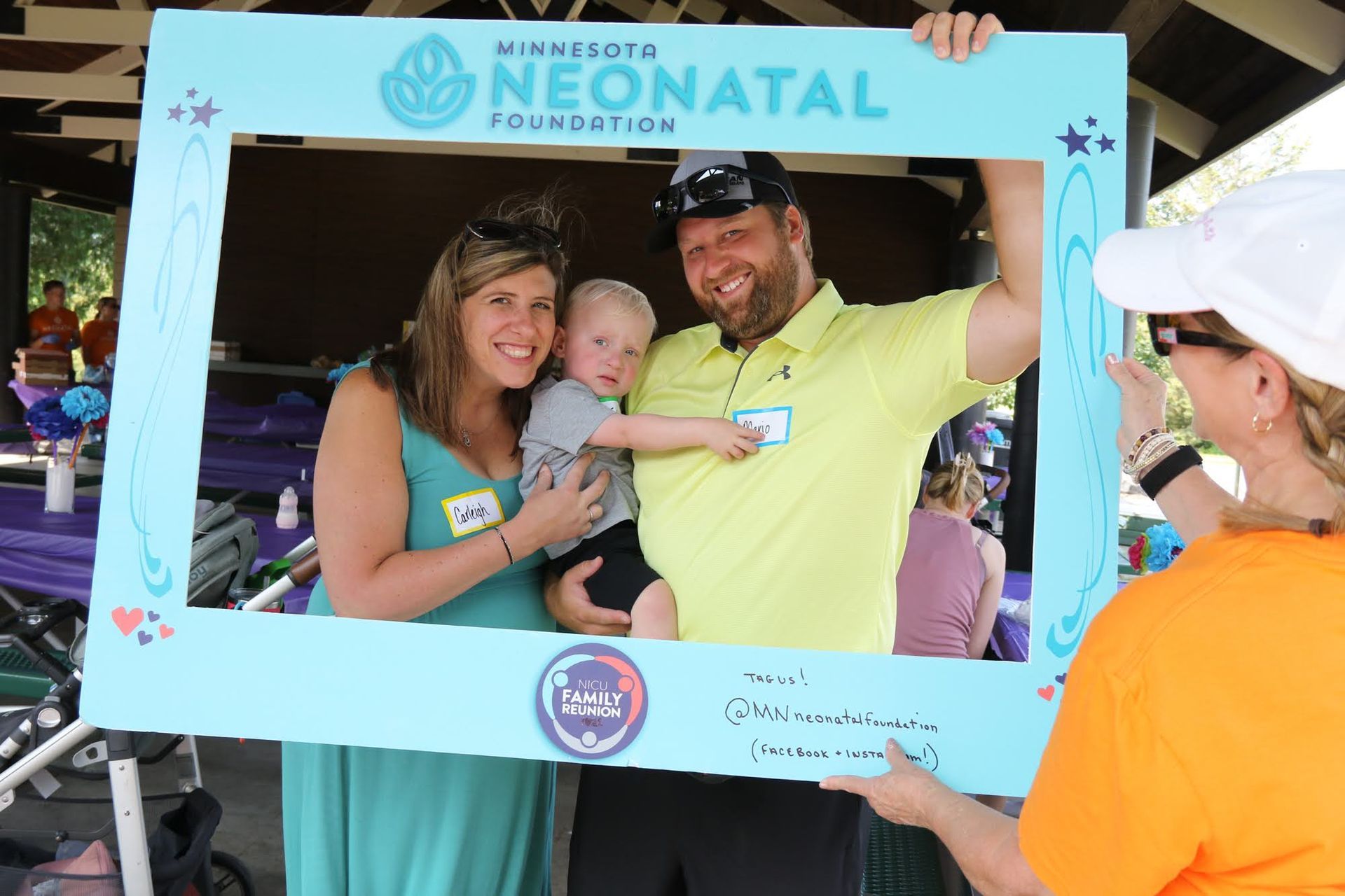 Family of three posing with a photo frame at an event; woman taking picture.