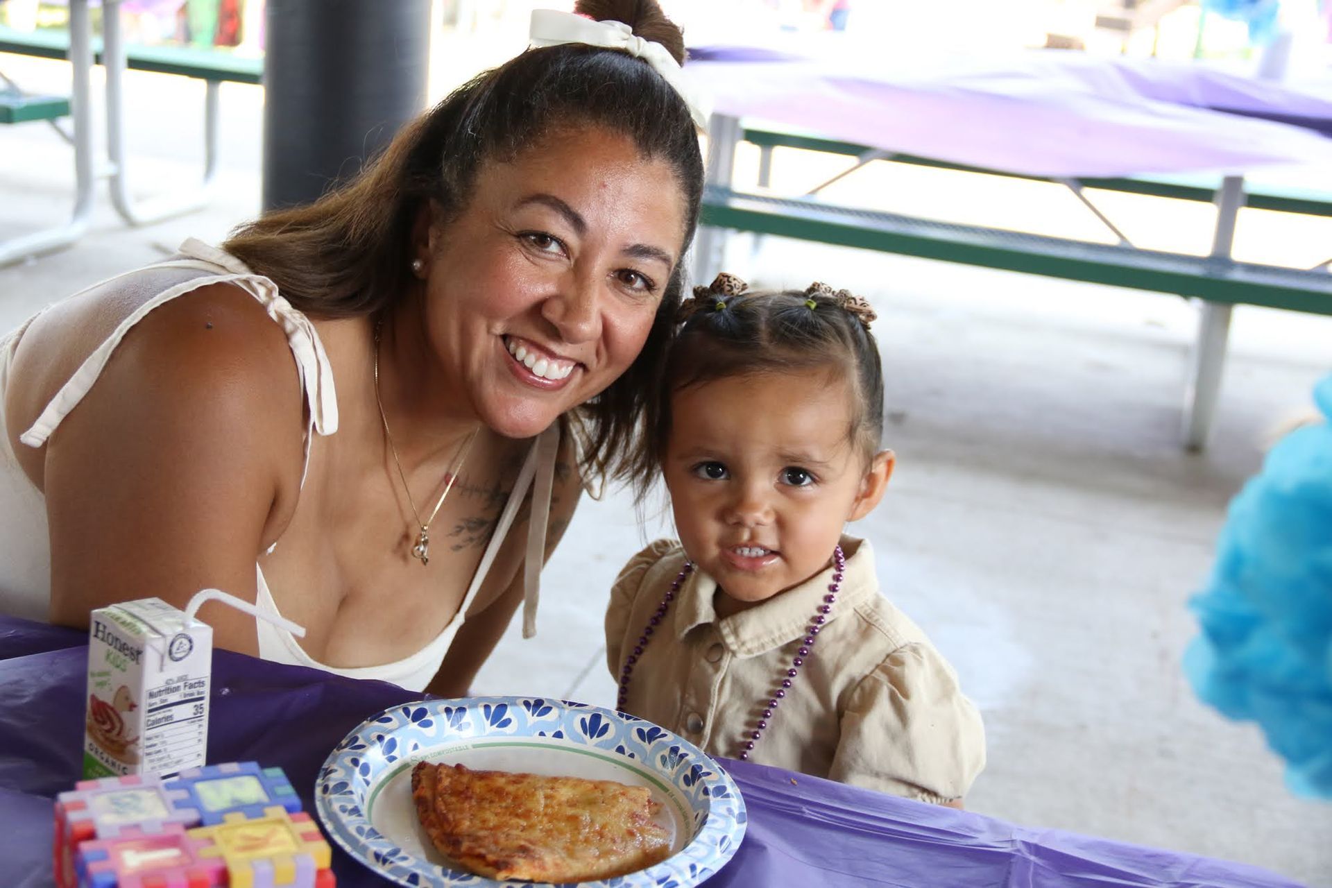 Woman and child smiling at a table with food, juice, and decorations at an outdoor event.