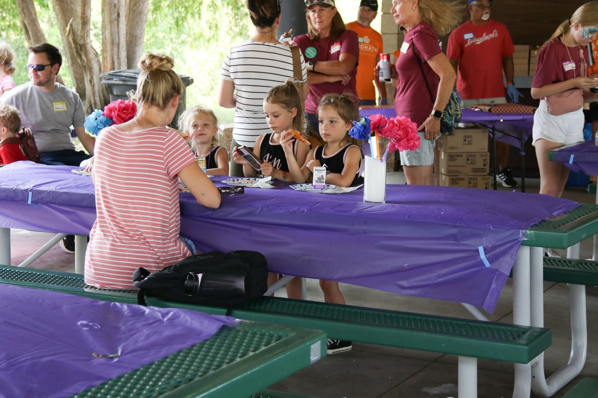 People at a picnic, including children, seated at tables with purple tablecloths.