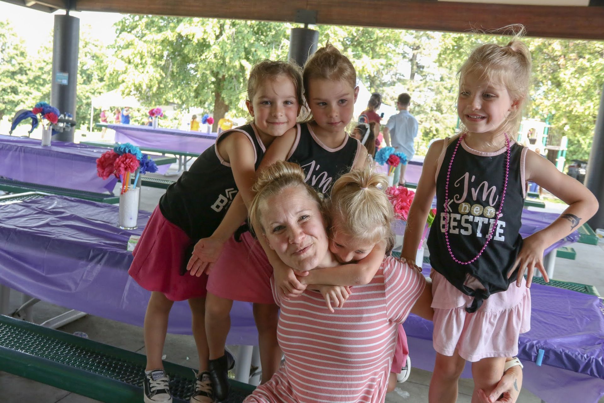 Woman surrounded by four young children at a park, smiling.