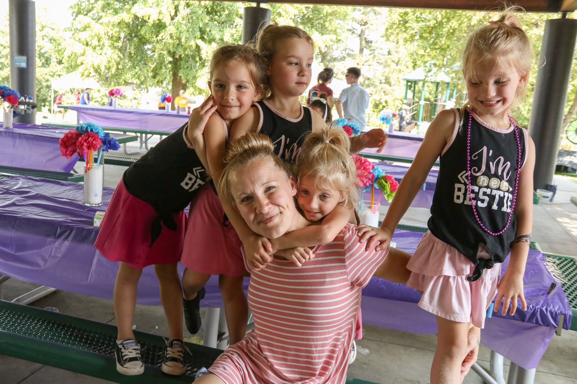 Woman surrounded by four young girls smiling at a party under a pavilion.