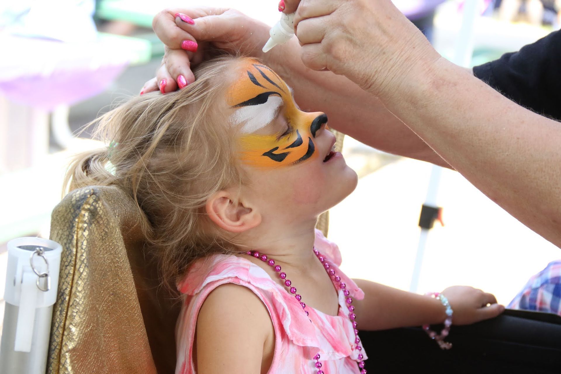 Girl getting tiger face paint applied outdoors.