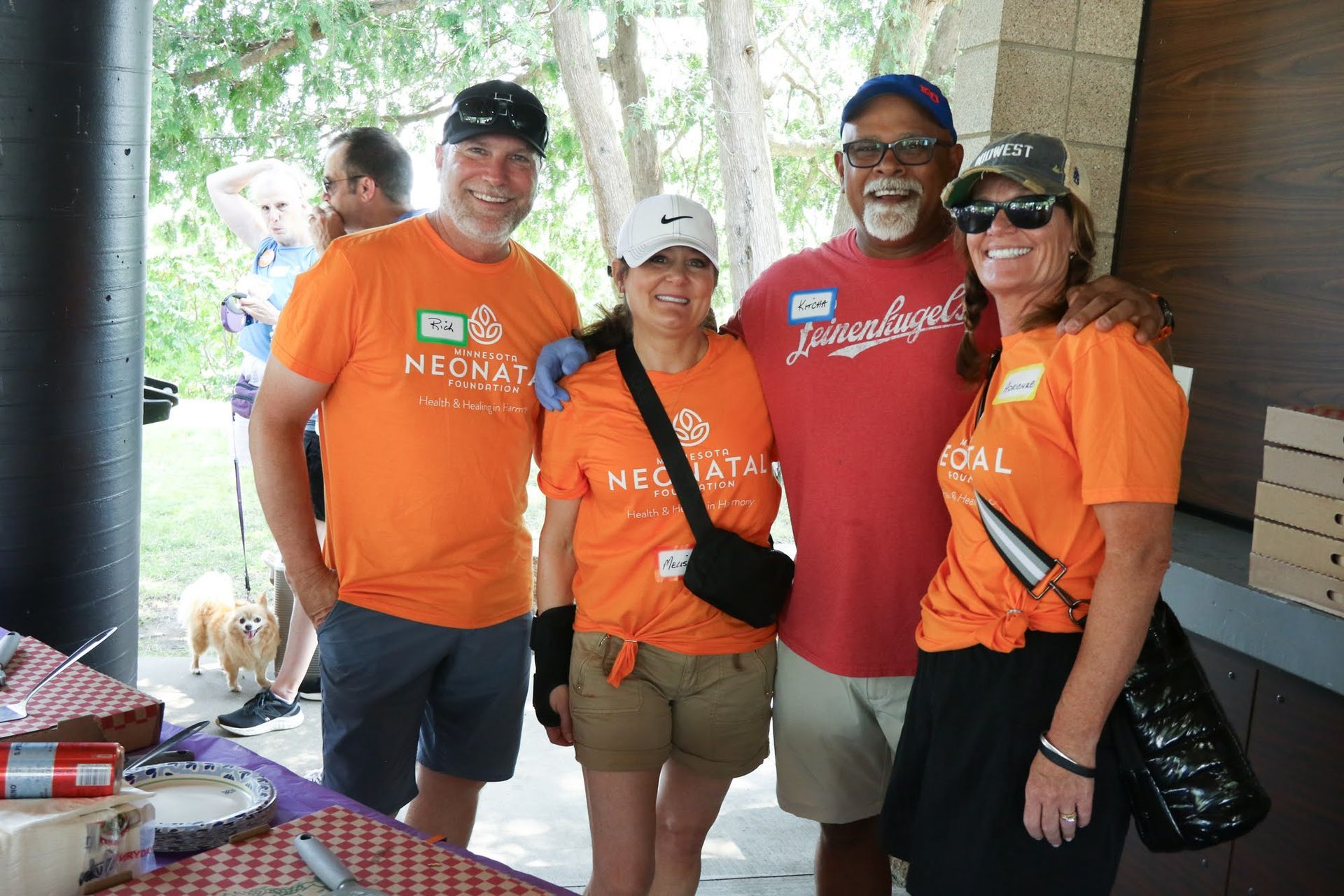 Four people in orange shirts pose for a photo outdoors.