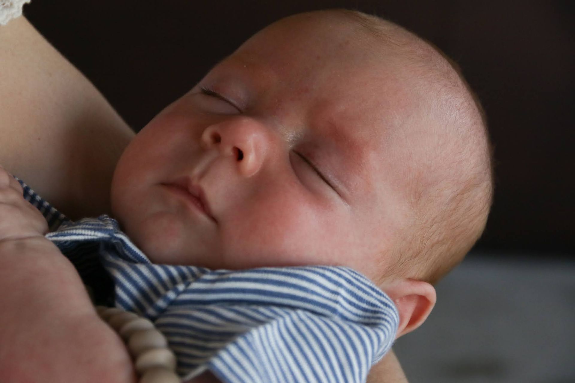 Sleeping baby held in arms, wearing blue and white striped shirt.