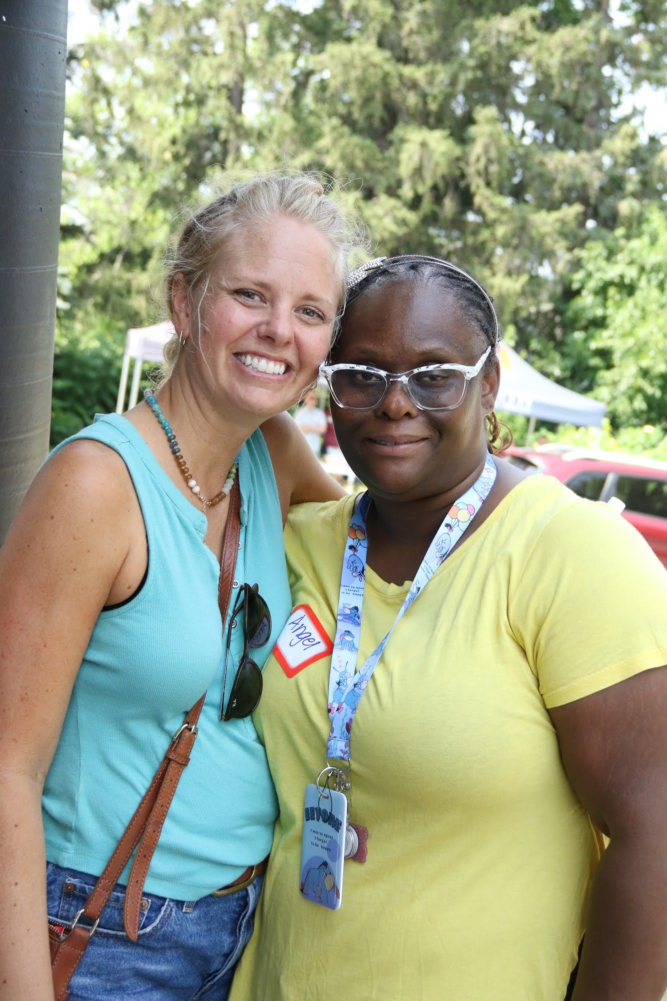 Two people smiling, outdoors; one with a blue top, the other in yellow, both wearing accessories.