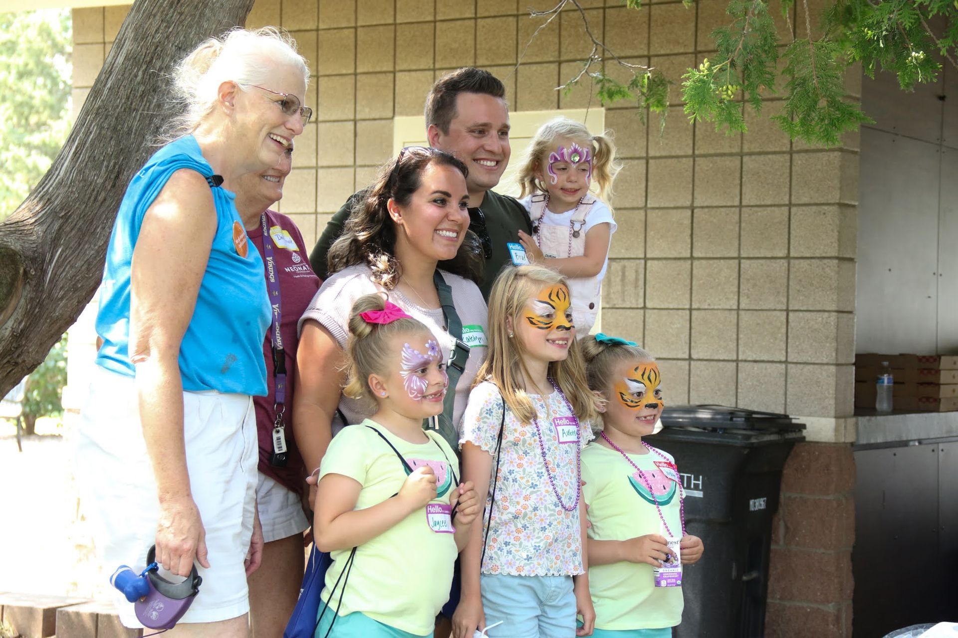 Group photo: People with face paint pose outdoors. Some children are smiling.