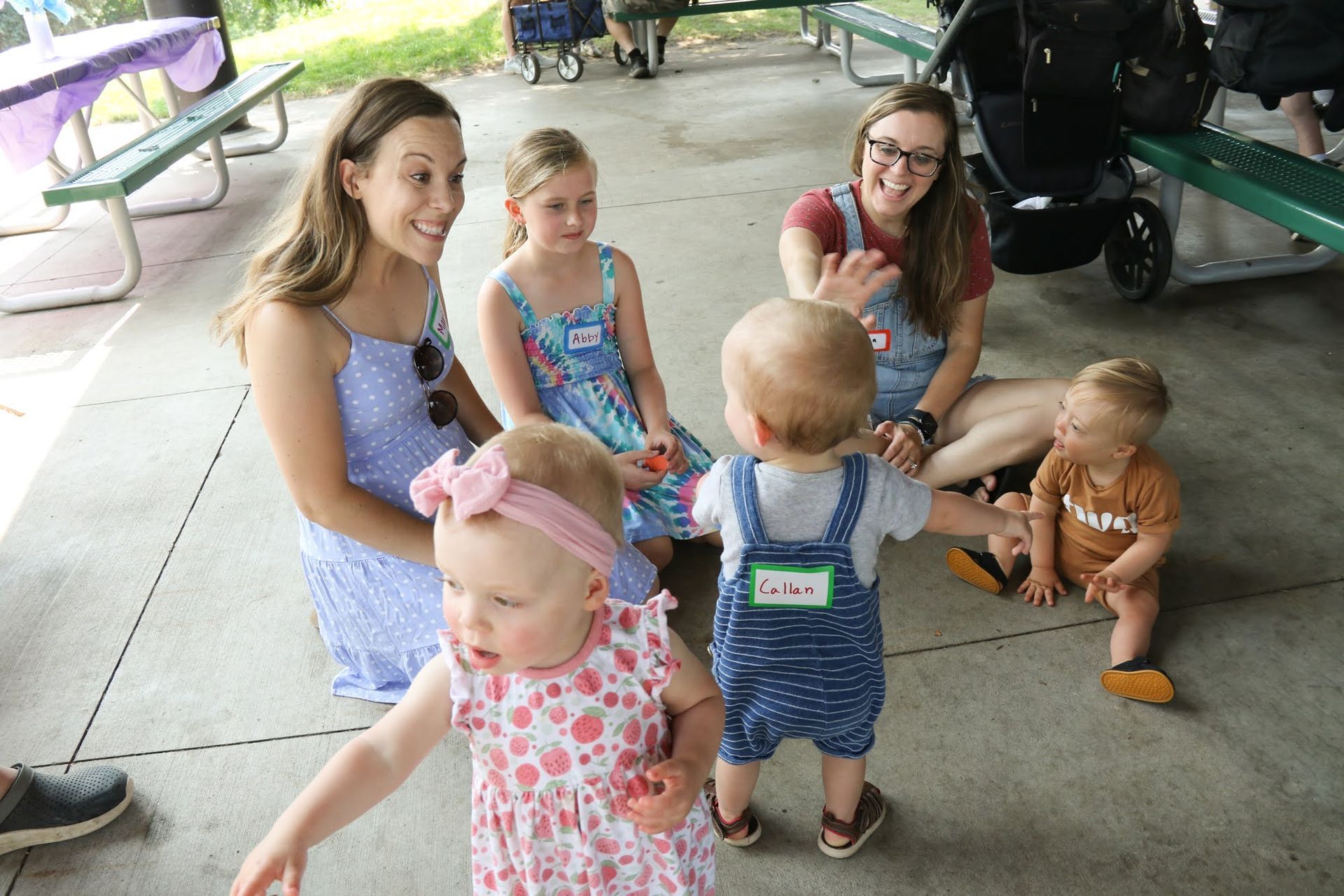 Group of people and children at a picnic. Two women, three small children, and a young girl seated near a picnic table.