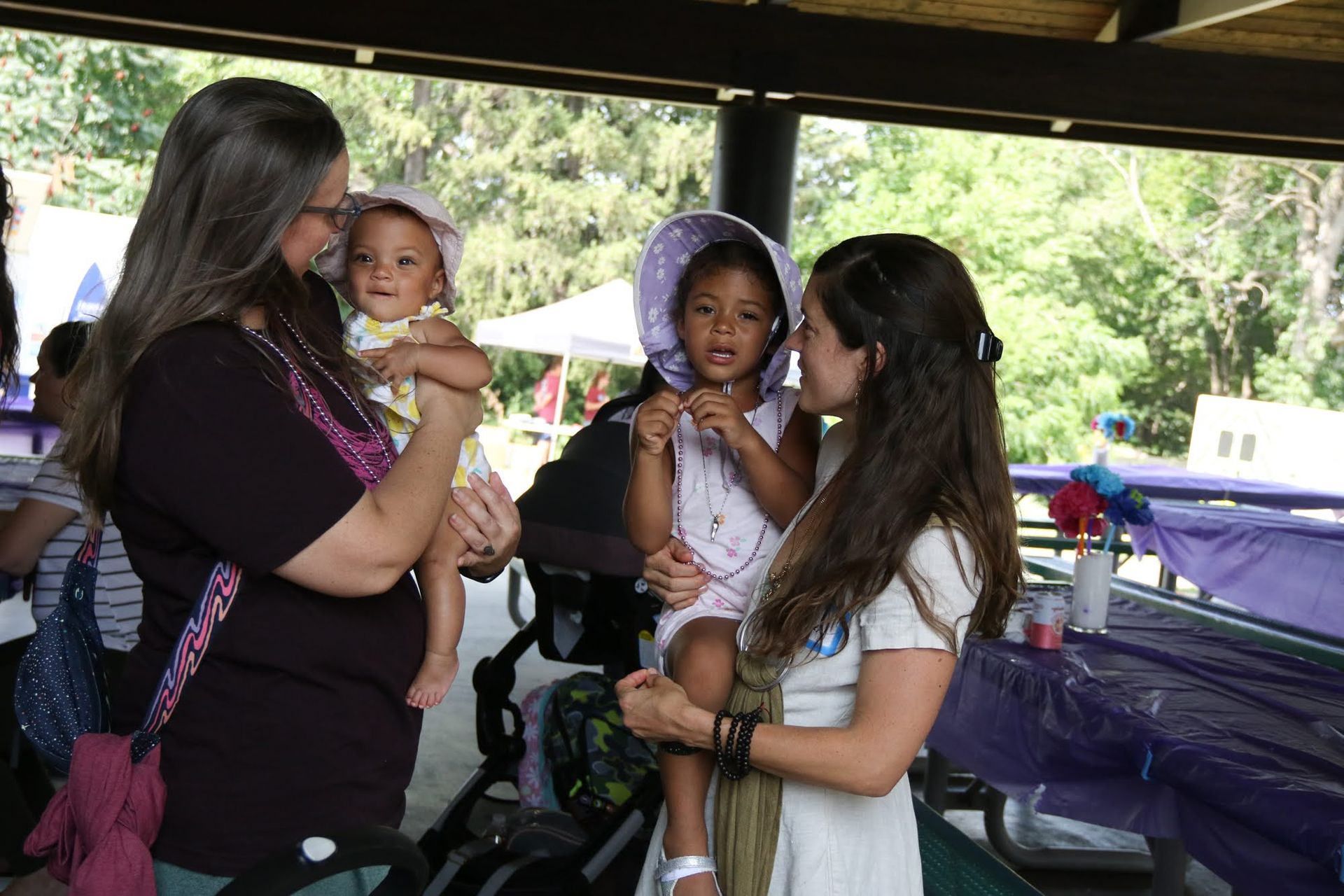 Two women and two children under a park shelter, looking at each other.