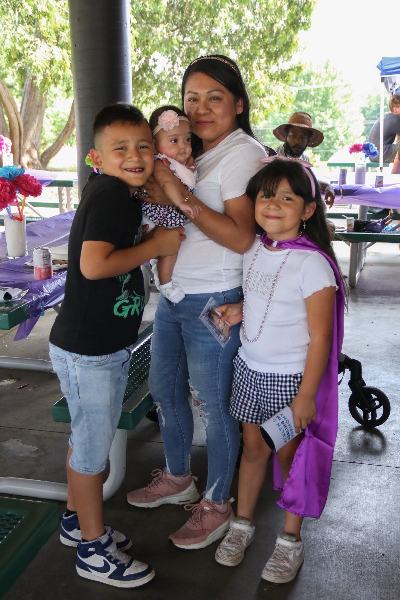 Woman holding baby poses with two children under a park shelter.