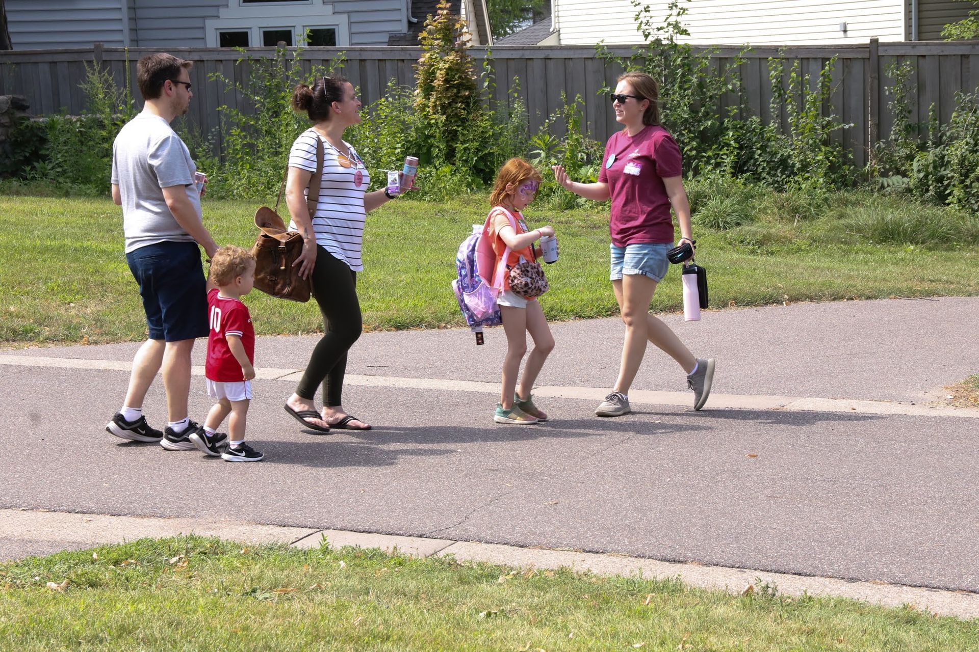 People walking on a paved path. A family of four with a guide, walking near grass and a fence.
