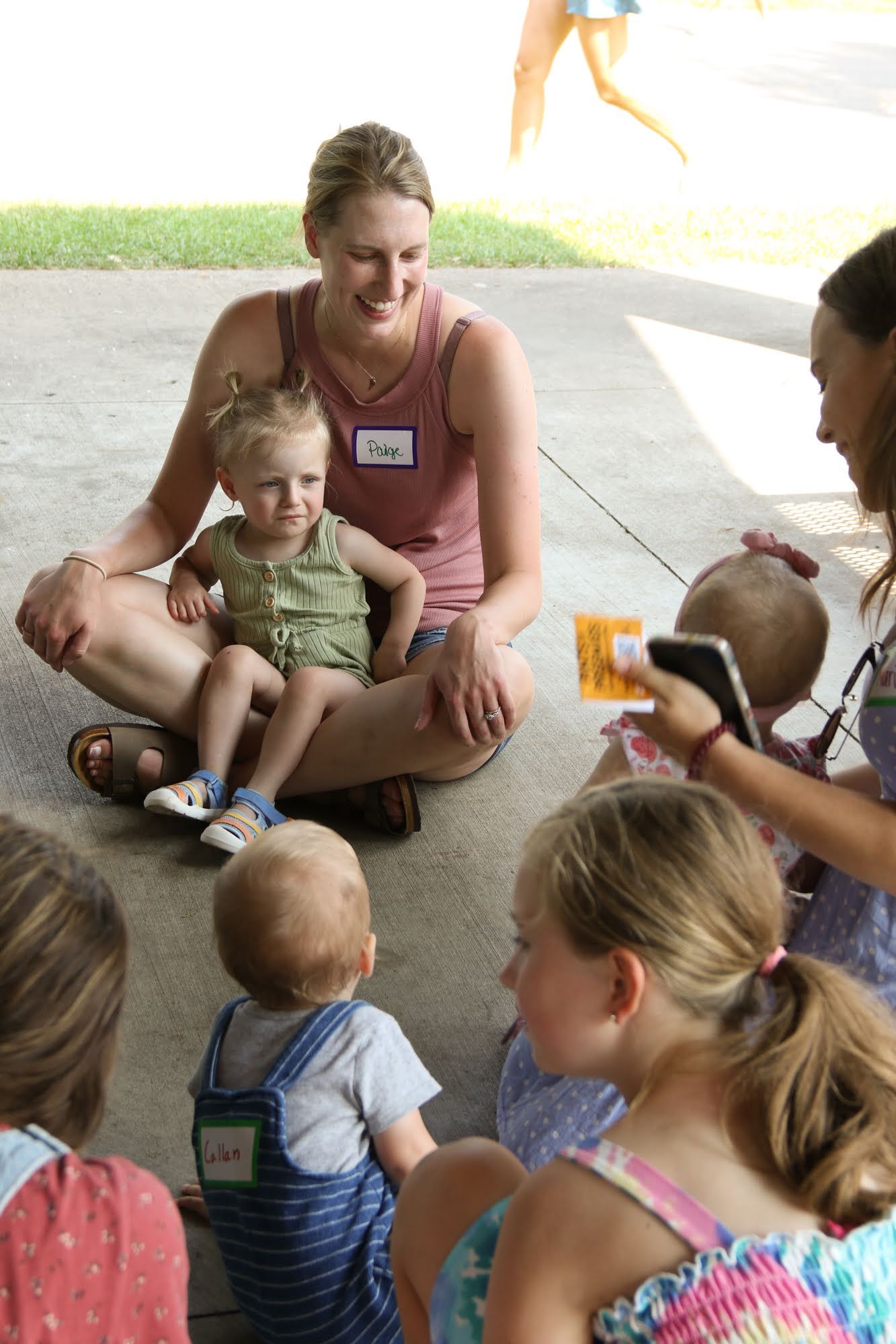 Woman seated with child, reading to a group of children under a pavilion.