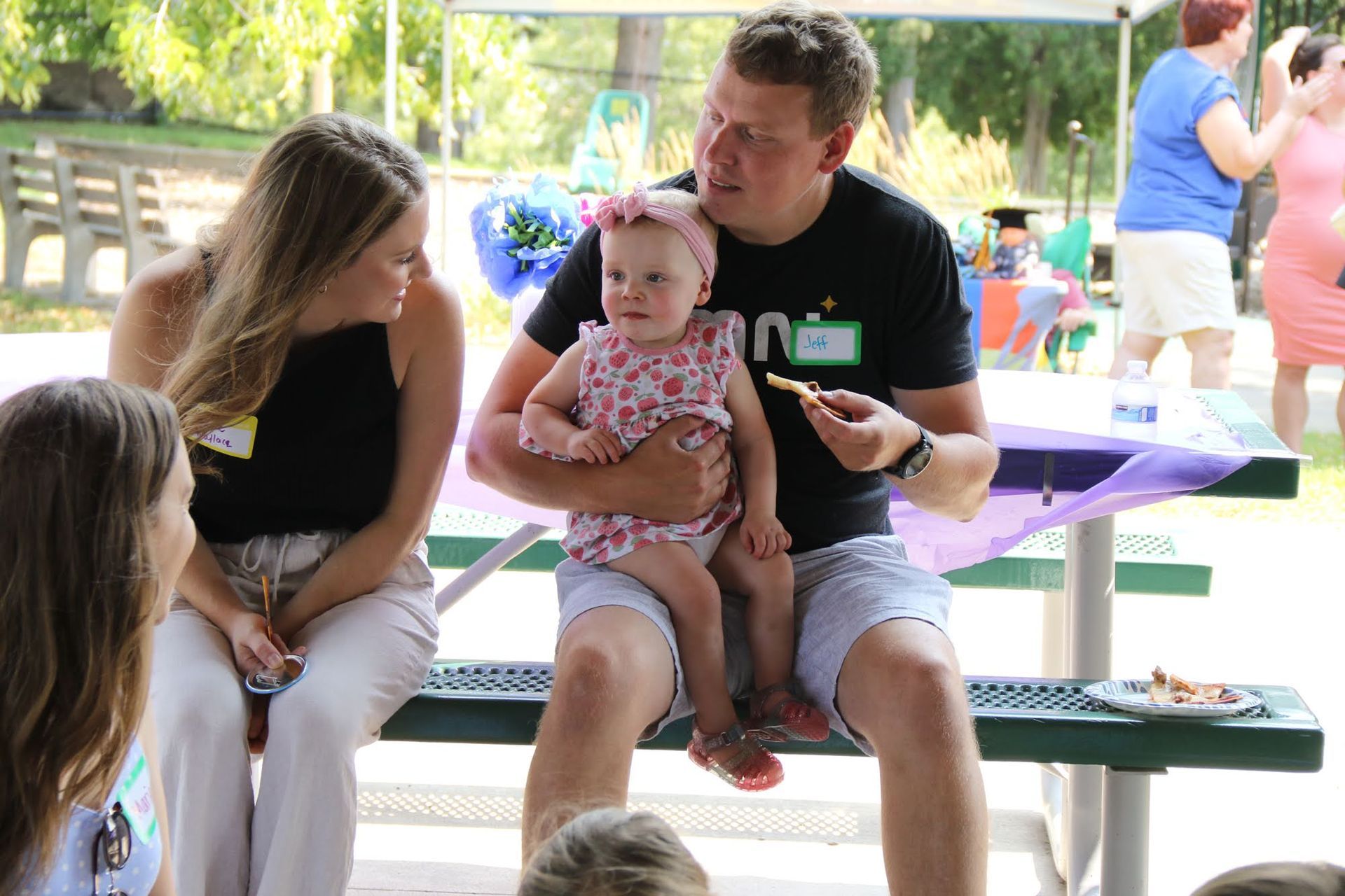 A man holds a baby in his lap while a woman sits beside them at an outdoor event.