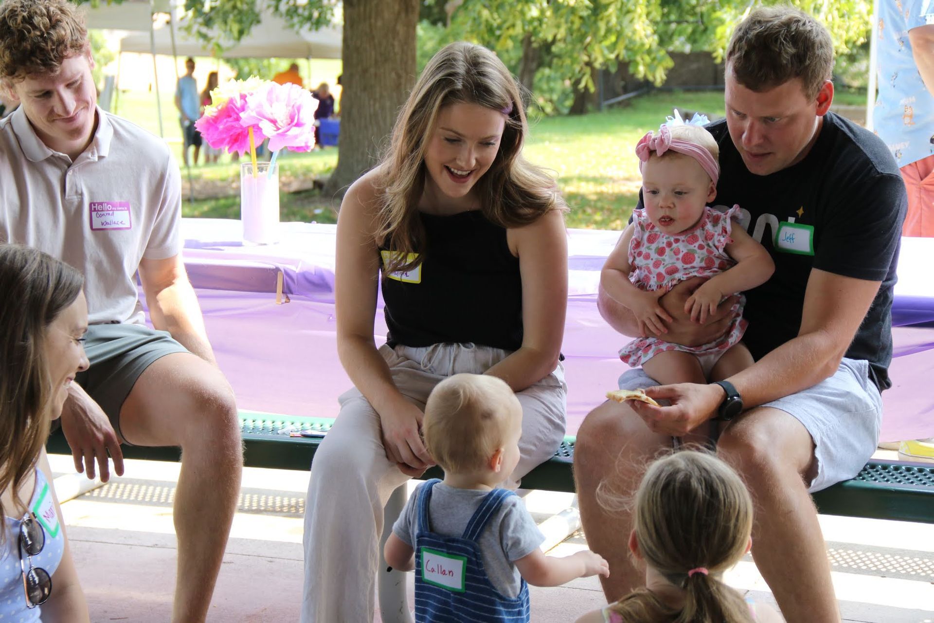 Group of people at an outdoor gathering, interacting with two babies.