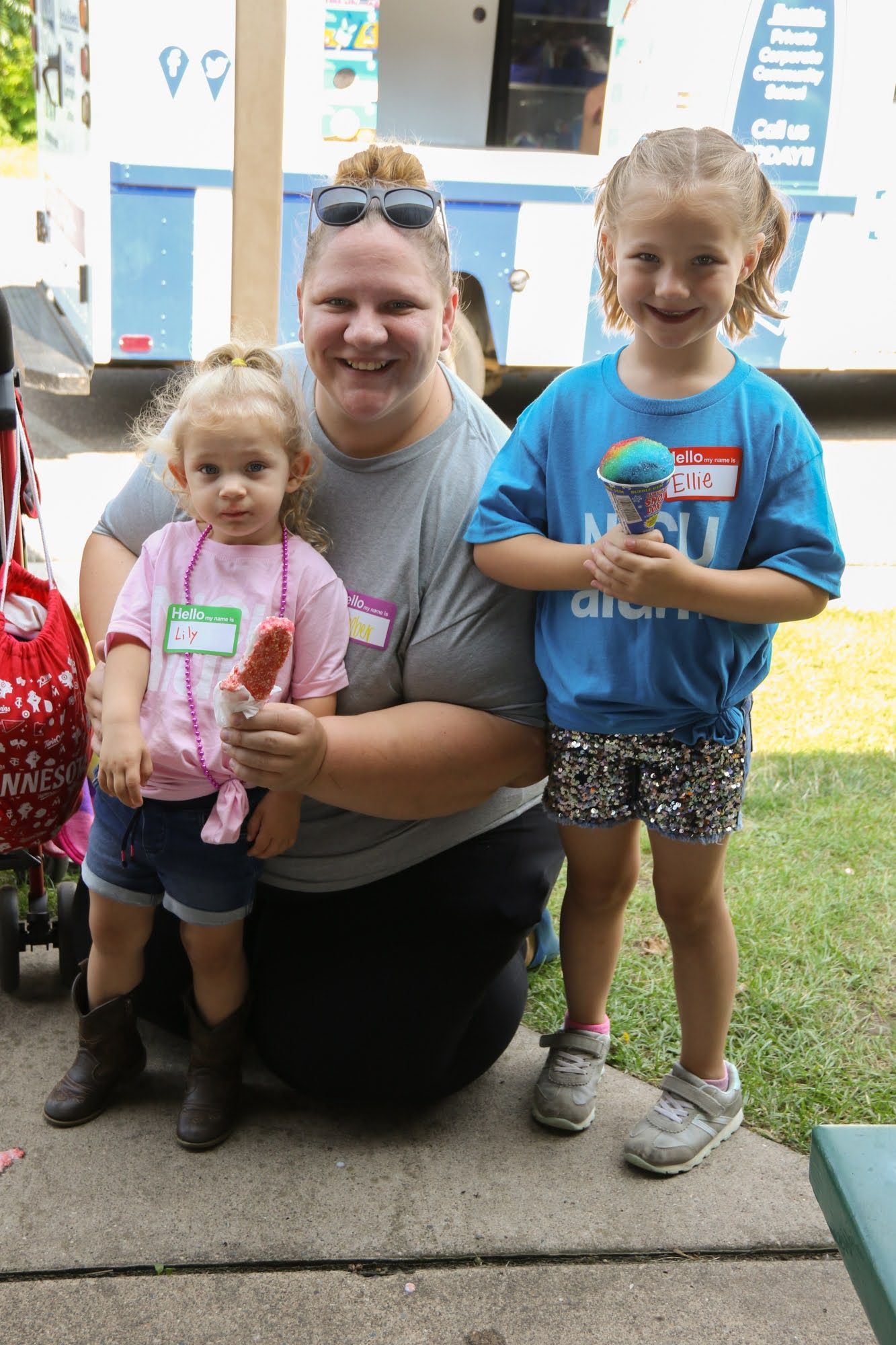 Woman with two young children smiling, holding treats, in front of an ice cream truck.