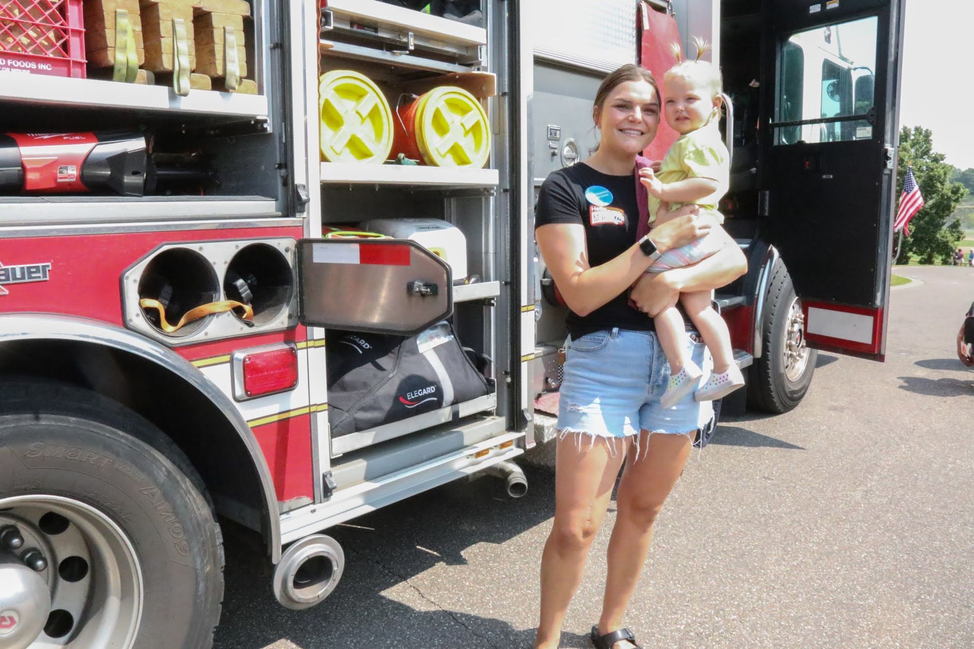 Woman holding a child in front of a fire truck with open storage compartments.