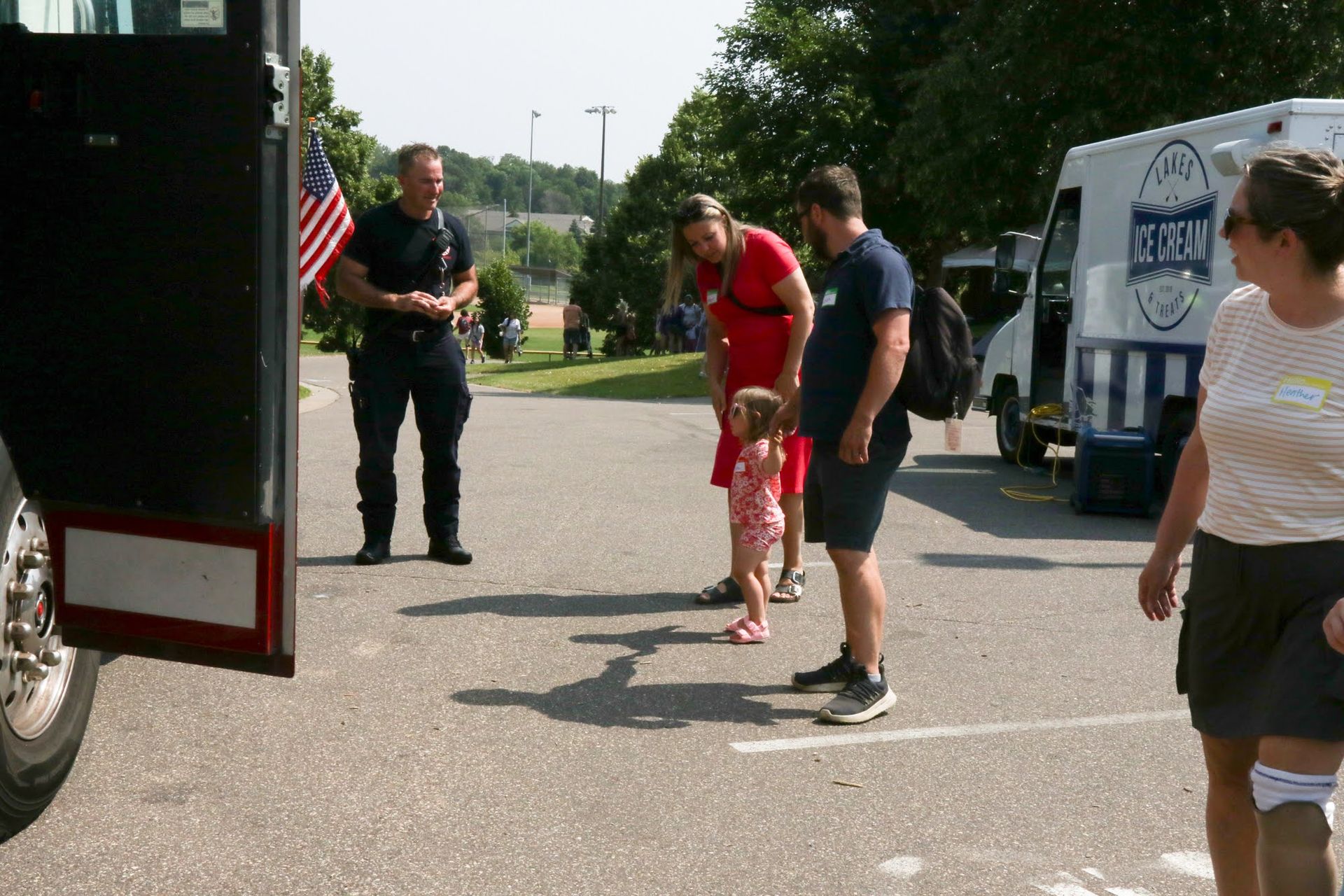Firefighter with family by an emergency vehicle and an ice cream truck outdoors.