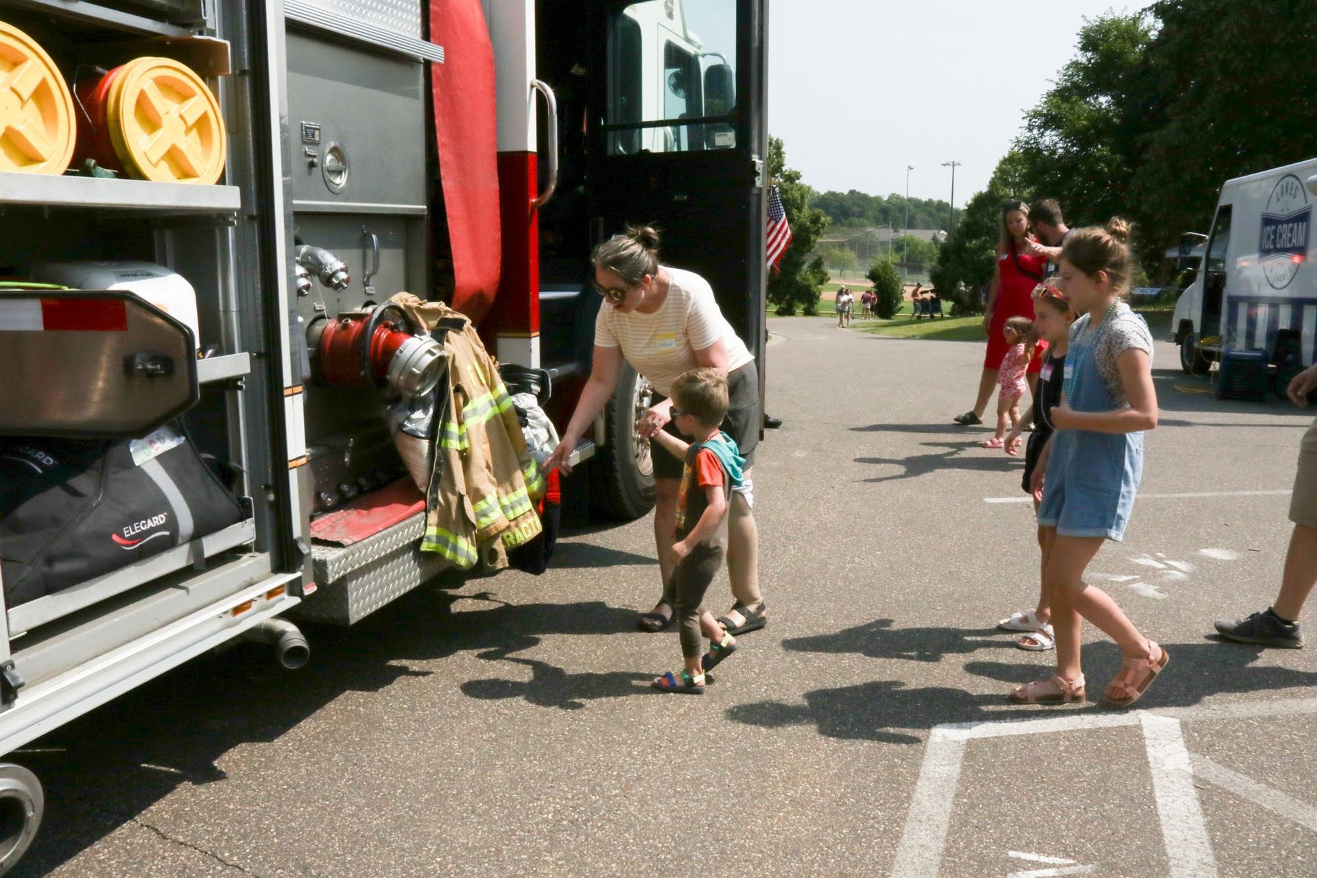 Woman shows firefighting gear to children at a parked fire truck.