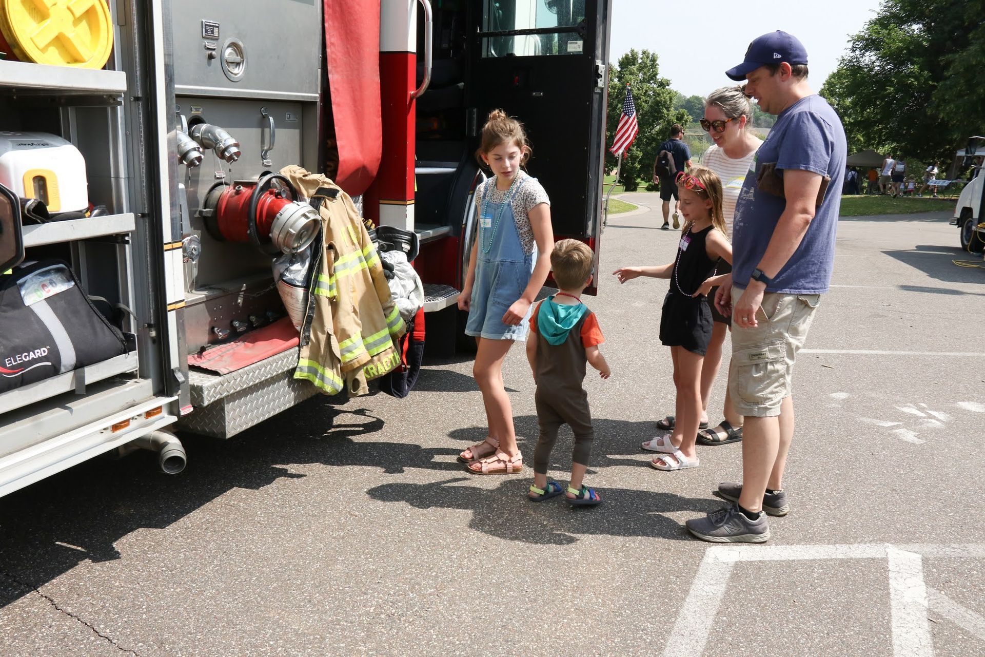 Family looking at equipment on a fire truck in a parking lot. Child pointing.