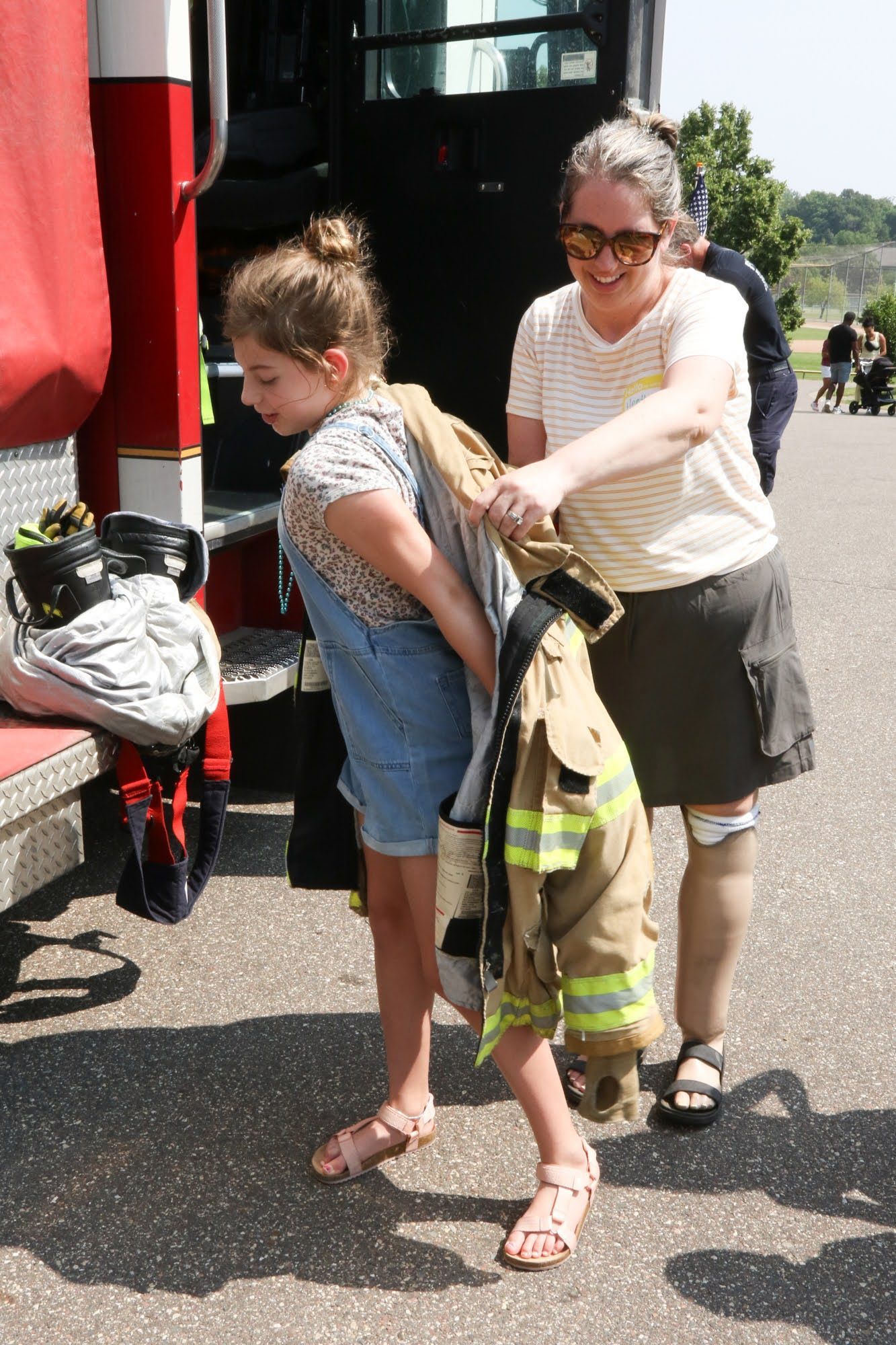 Woman helping a child put on firefighter gear near a fire truck.
