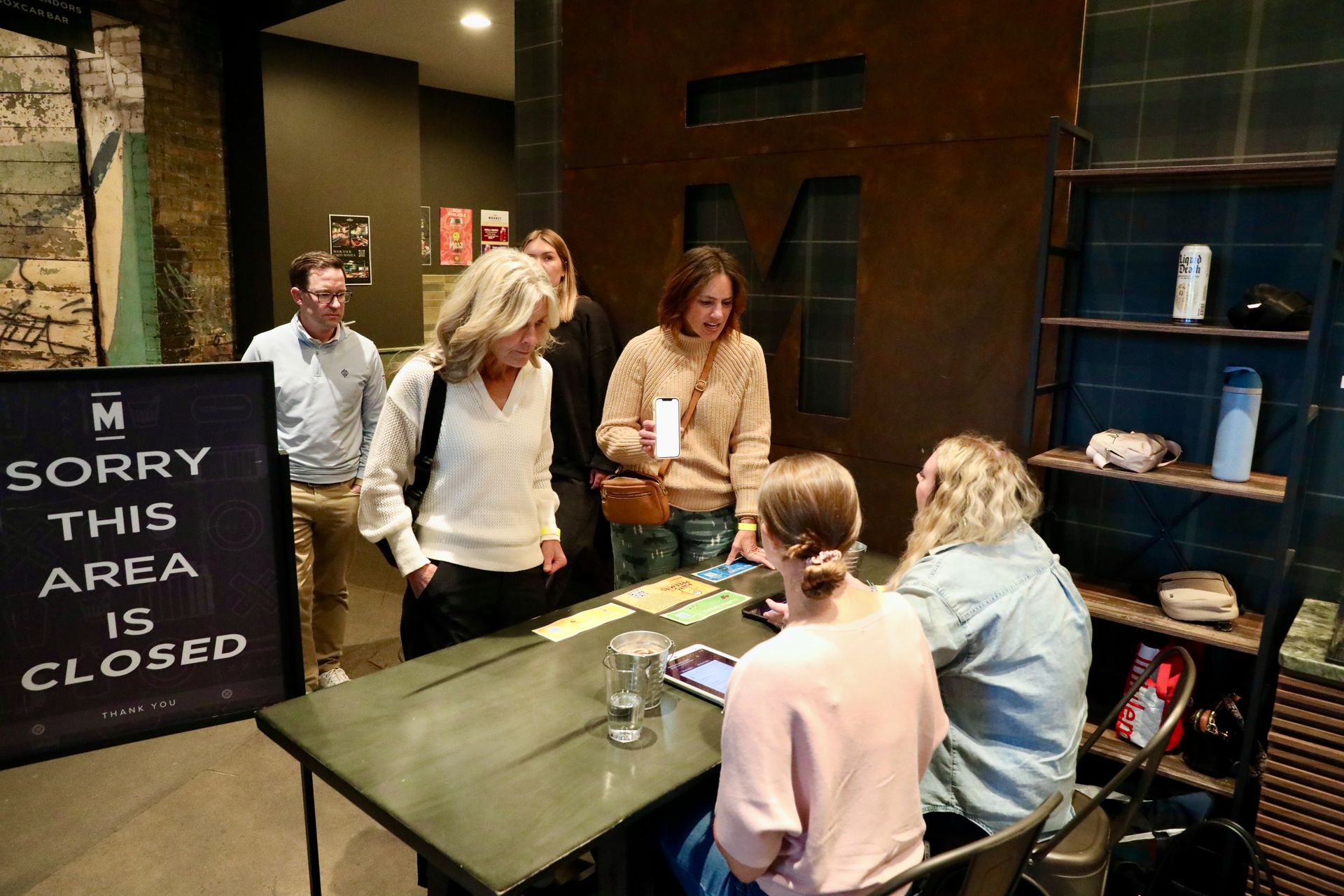 People at a closed area entrance, some talking to two seated people behind a table. 