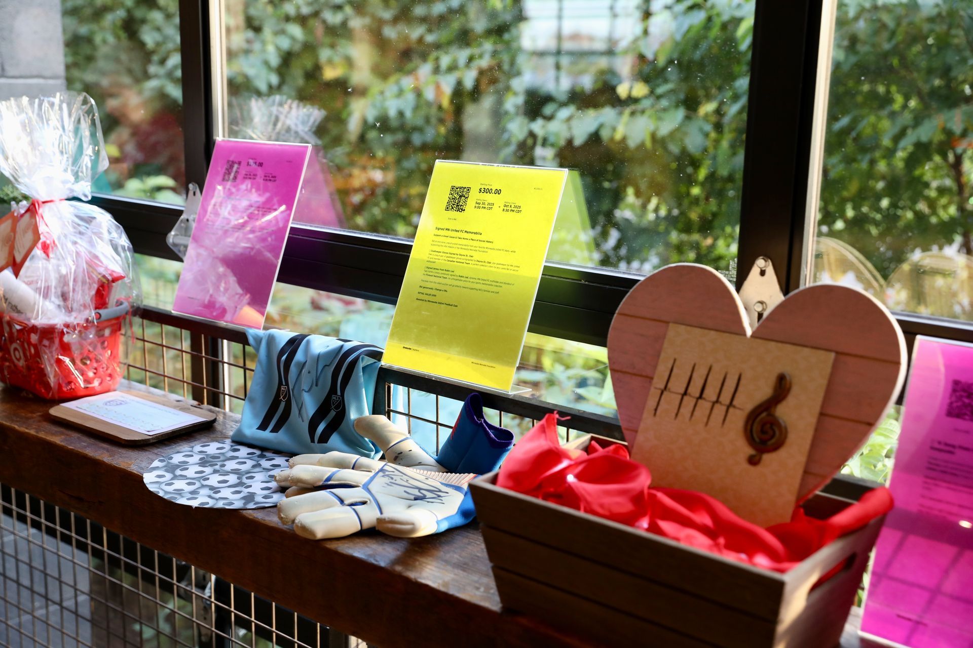 Display of gifts and cards on a wooden ledge, including a heart-shaped item, wrapped basket, and colorful cards near a window.