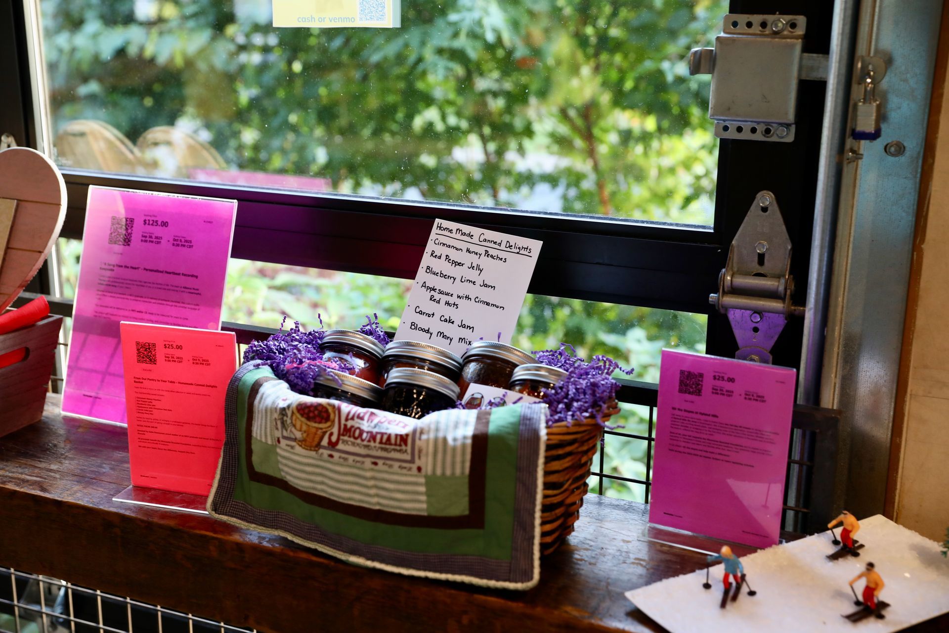 A basket of jars with purple flowers sits on a windowsill next to pink signs and a small ski scene.