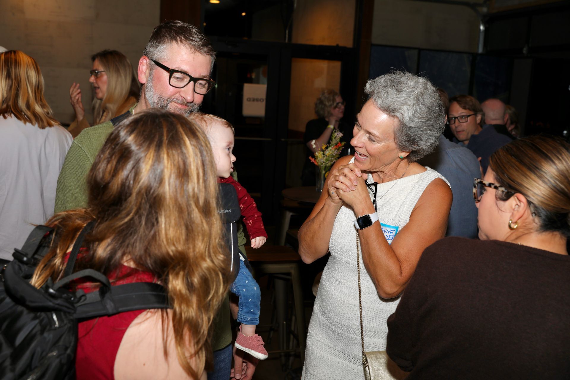 People conversing indoors; woman speaking with a microphone, others listening.