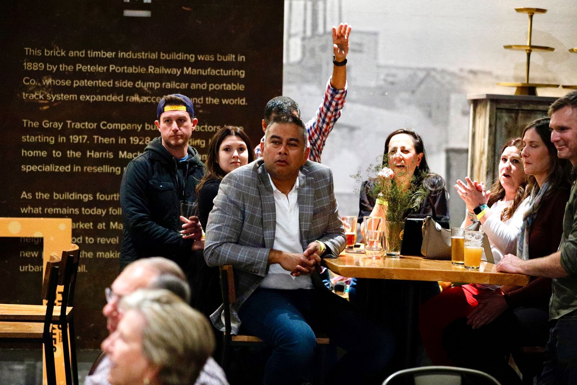 People in a room with a bar, celebrating. One person raises their arm.