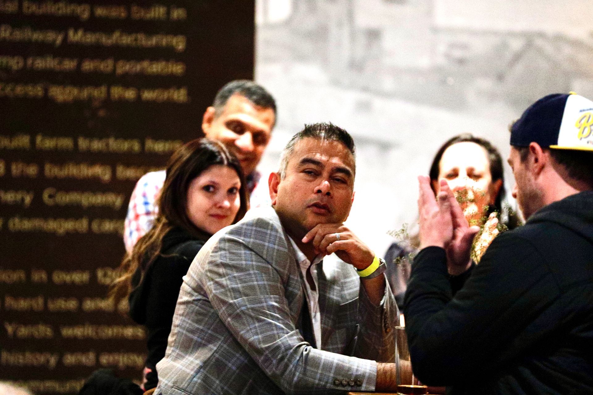 Group of people at a gathering; man in blazer looking at camera.