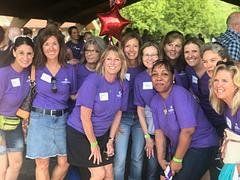 Group of people wearing purple shirts, smiling outdoors, near a red balloon.