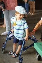 Boy in striped shirt and cap using a walker, smiling. Outdoors.