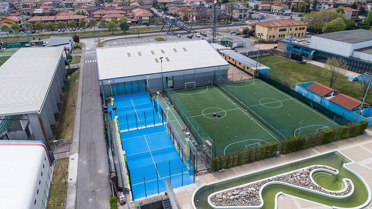 Vista aerea del complesso sportivo con campi da paddle blu, campi da calcio verdi e un edificio bianco.