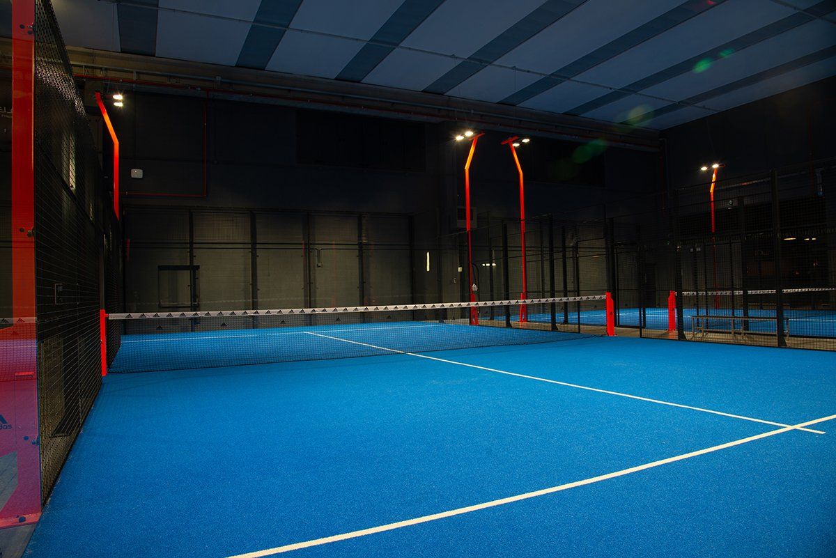 Campo da padel indoor con superficie blu e pareti nere. Linee, rete e strutture di supporto bianche.