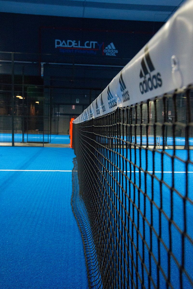 Campo da padel blu con rete, logo Adidas visibile.