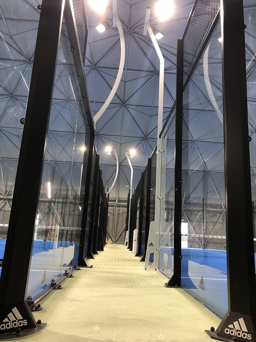 Campo da tennis coperto con reti nere, campi blu e illuminazione dall'alto.