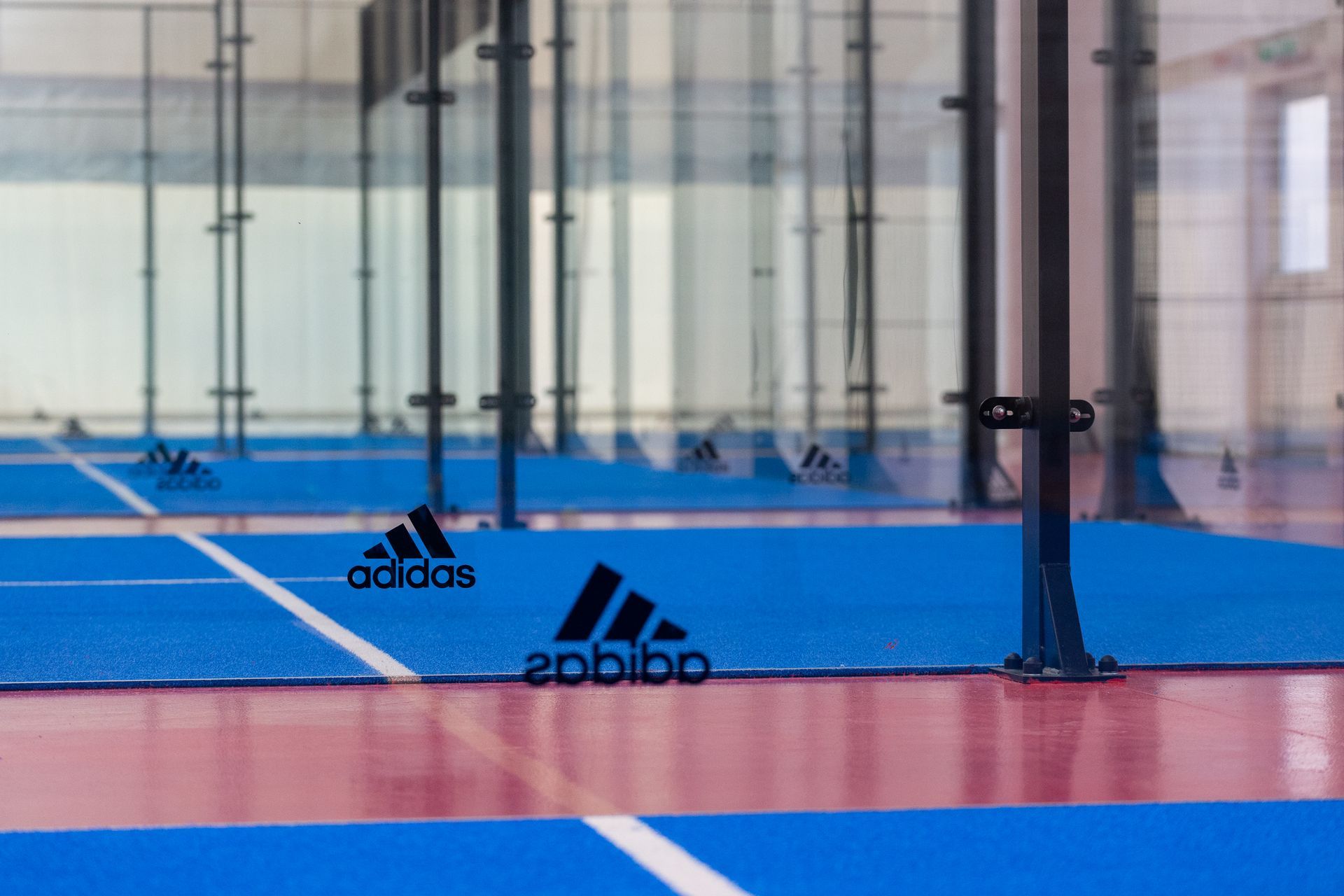 Campo da padel blu e rosso con pareti in vetro e logo Adidas.