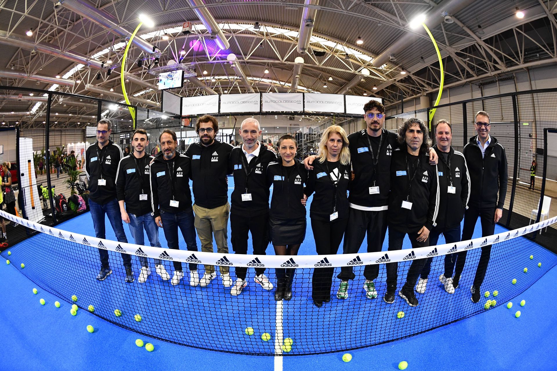 Gruppo di persone in abbigliamento Adidas nero in posa su un campo da padel