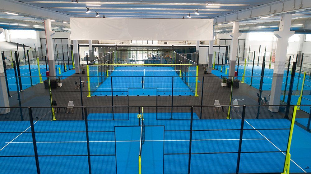 Campo da padel indoor con campi blu e recinzione nera e gialla.