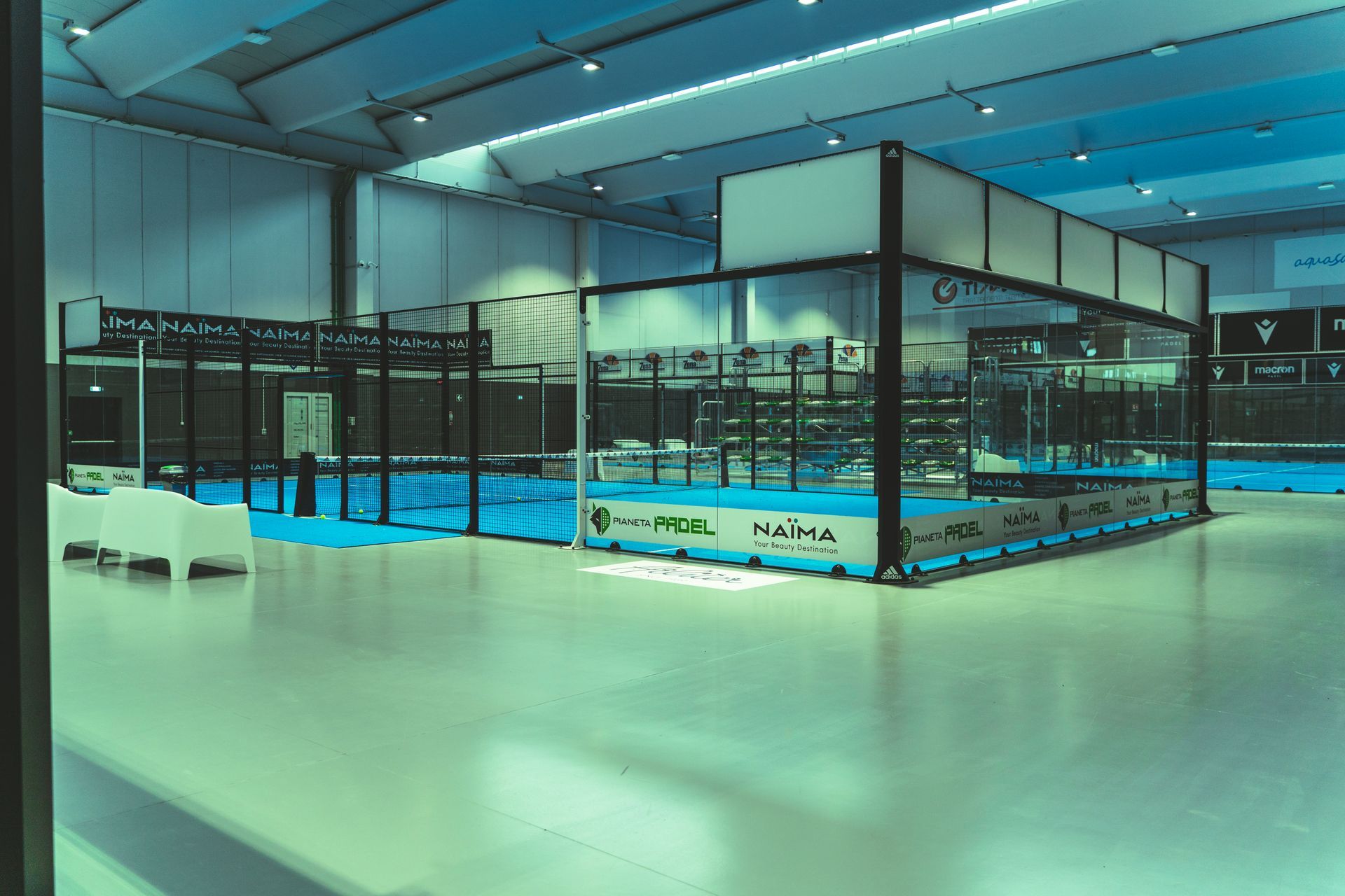 Campo da padel tennis al coperto con superficie di gioco blu e pareti in vetro.