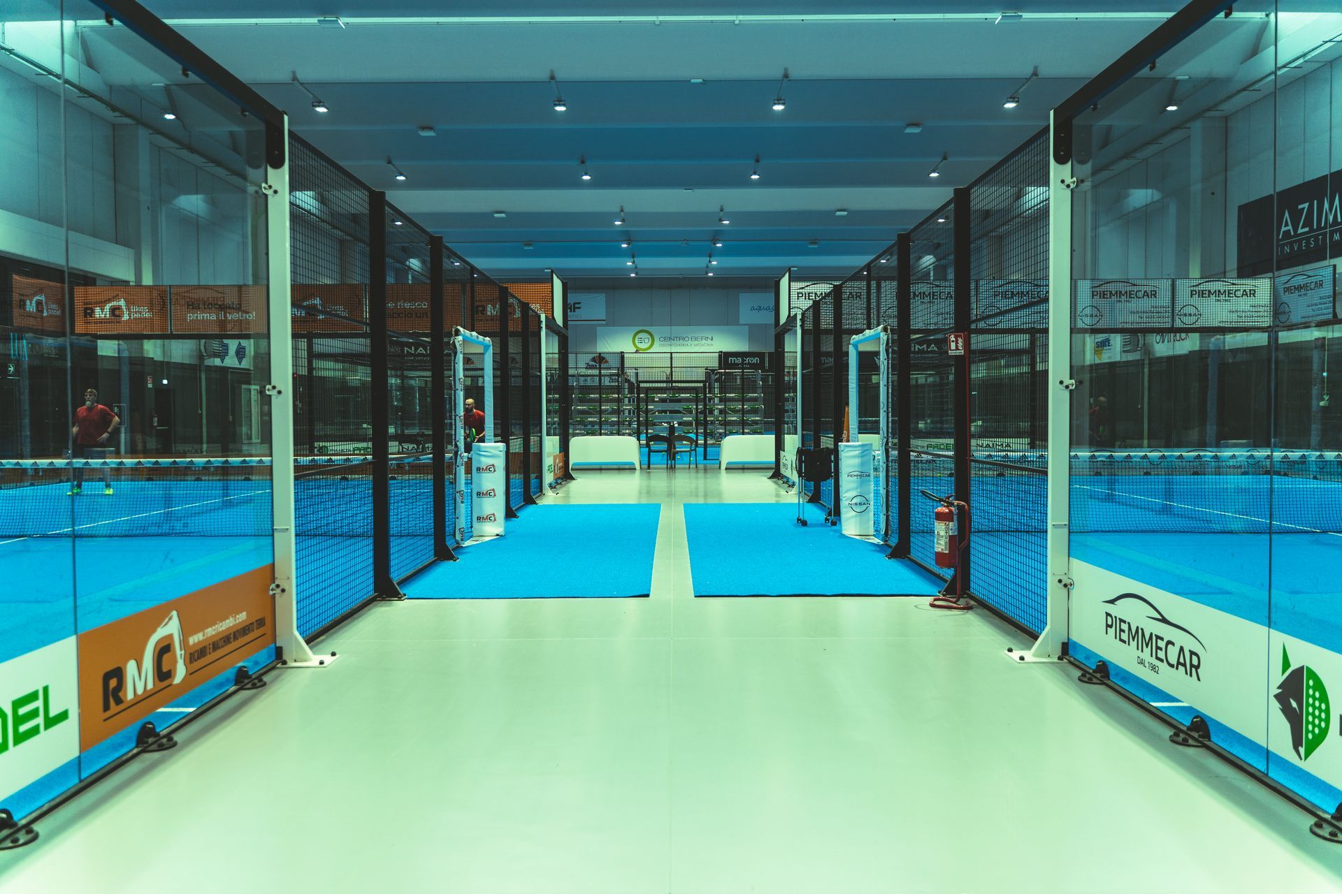 Campi da padel indoor con superfici blu e pareti in vetro.