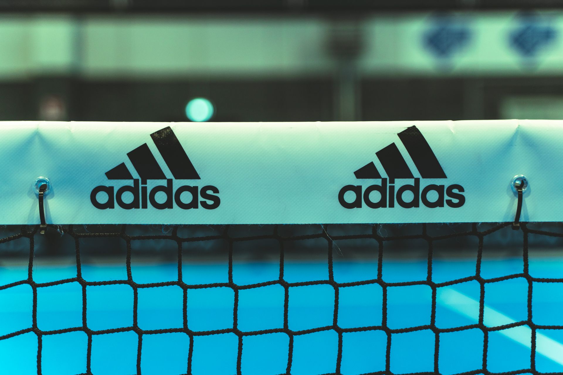 Logo Adidas su una rete da tennis blu e nera con sfondo turchese.
