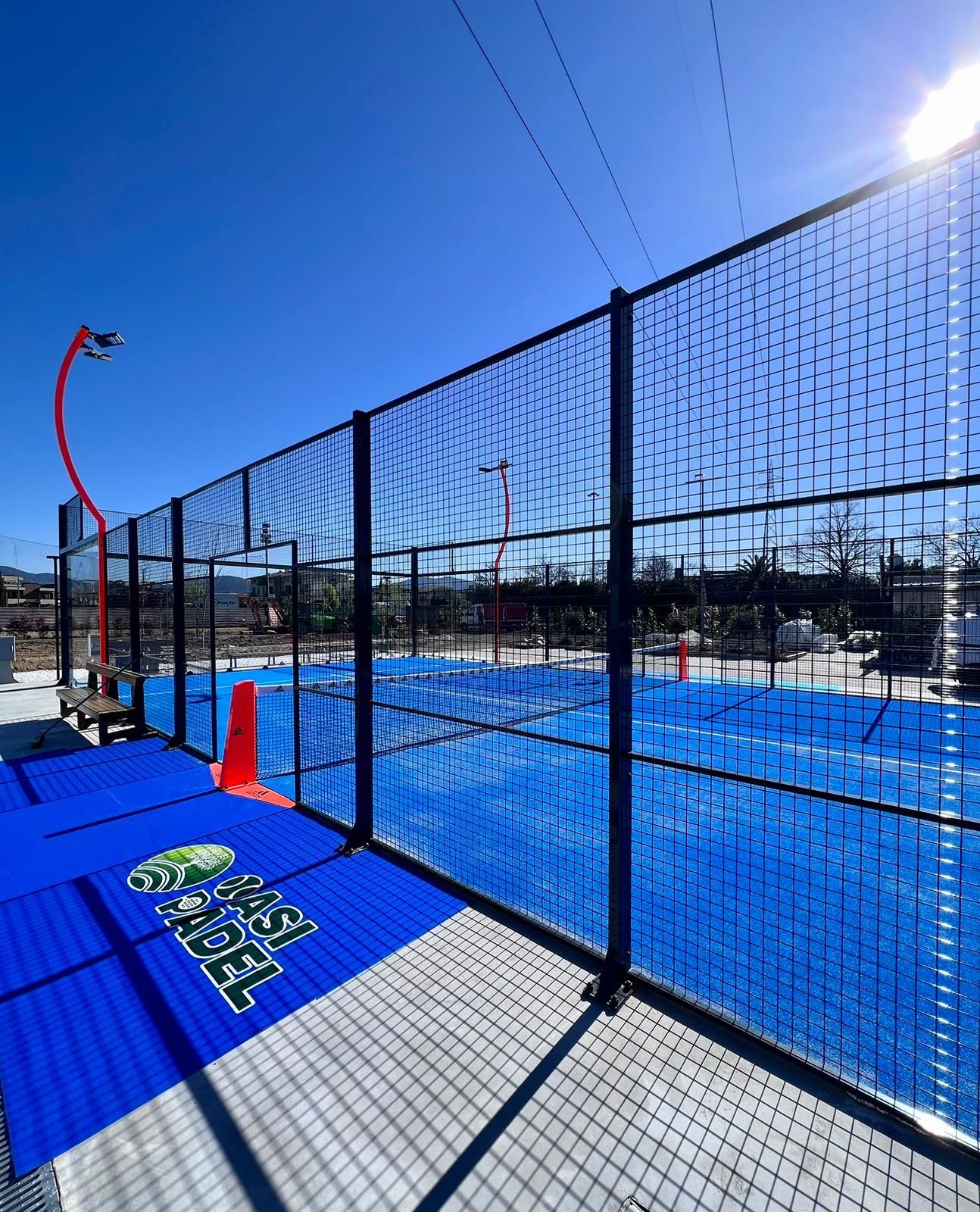 Campo da padel all'aperto blu e grigio con recinzione in una giornata di sole.