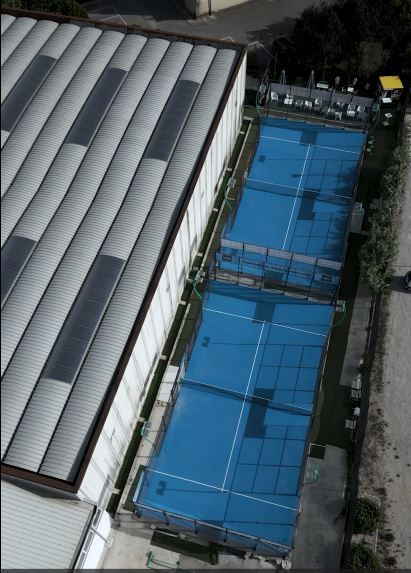Vista aerea di due campi da padel blu accanto a un edificio con il tetto grigio.