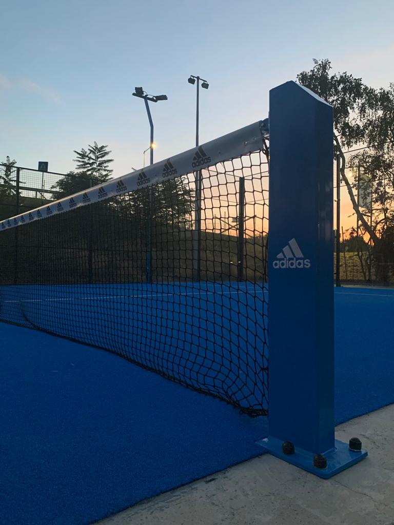 Rete da paddle tennis blu su un campo con il logo Adidas. Cielo al tramonto sullo sfondo.