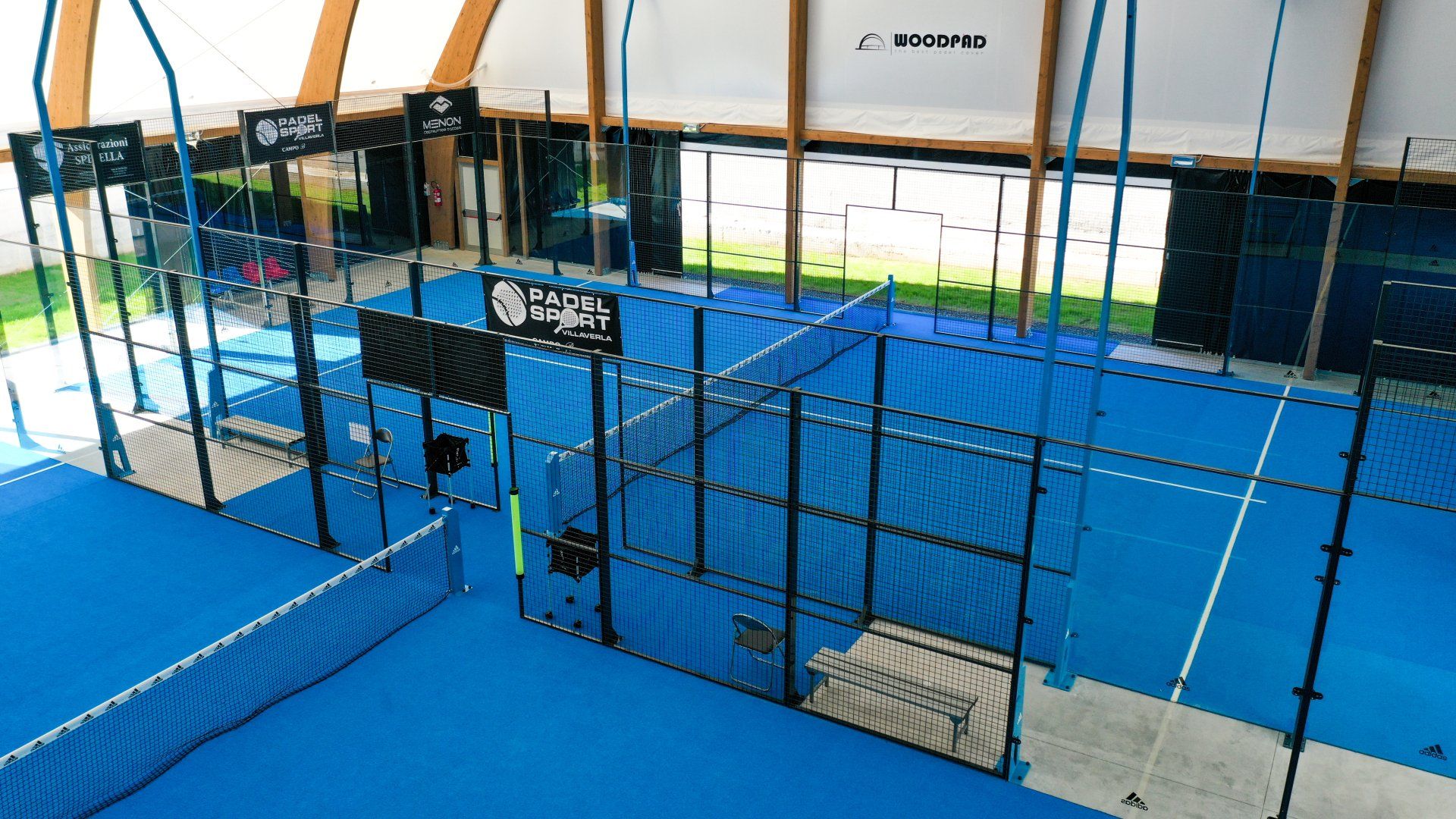 Campo da padel indoor con superficie blu e reti nere.